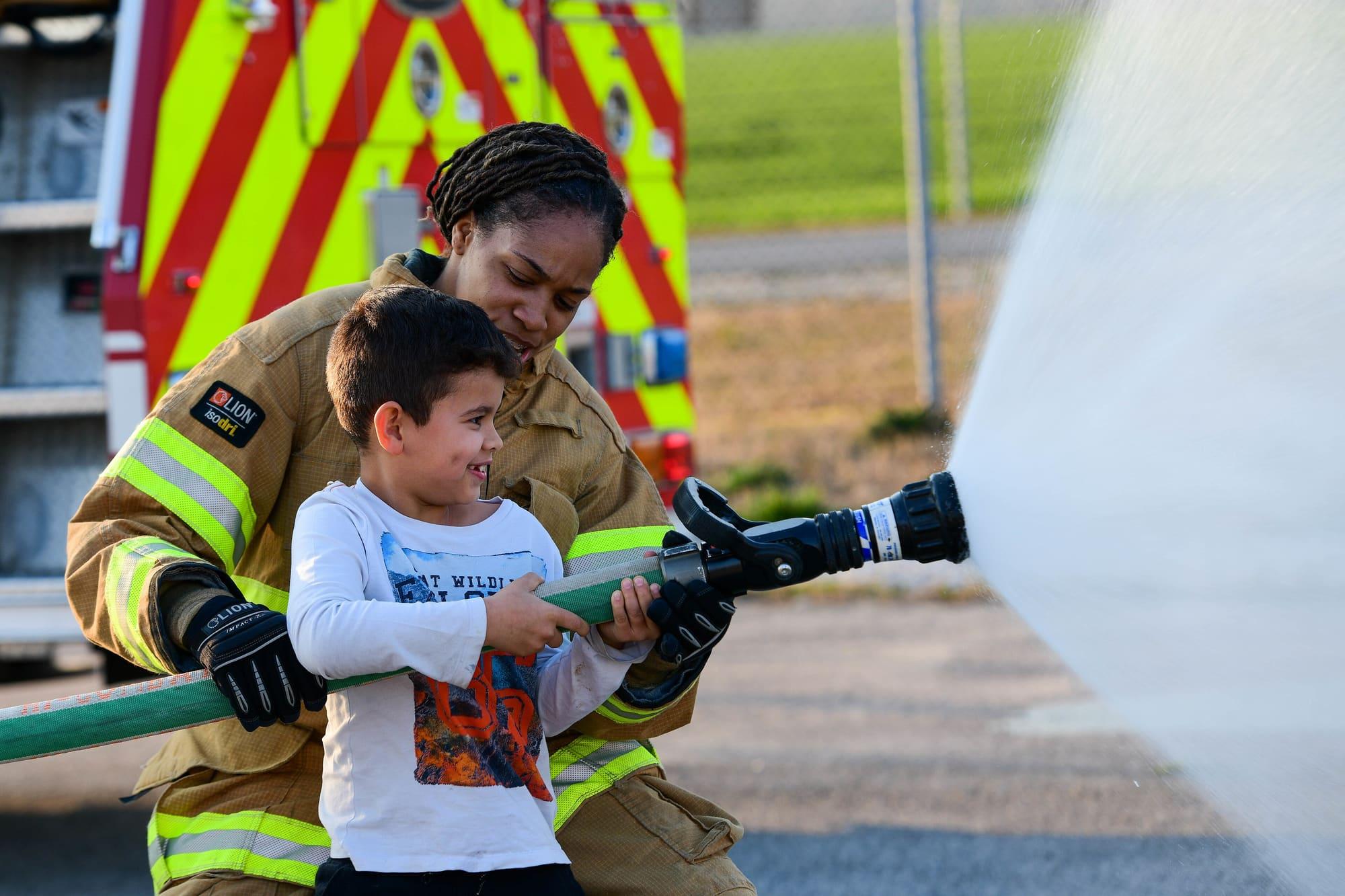 firefighter helping a child spray a fire hose